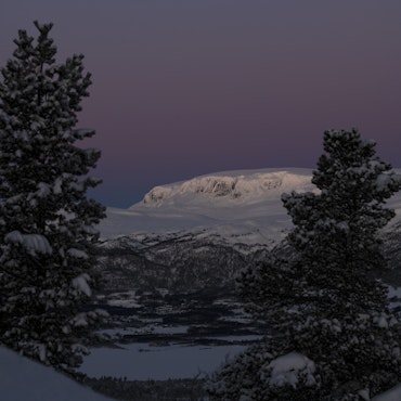 Winter scene in Hallingskarvet, Hallingdal Nonstølvegen, Hovet, Norway. Visible are a cozy chalet nestled amongst snowy peaks and an expansive mountain landscape.