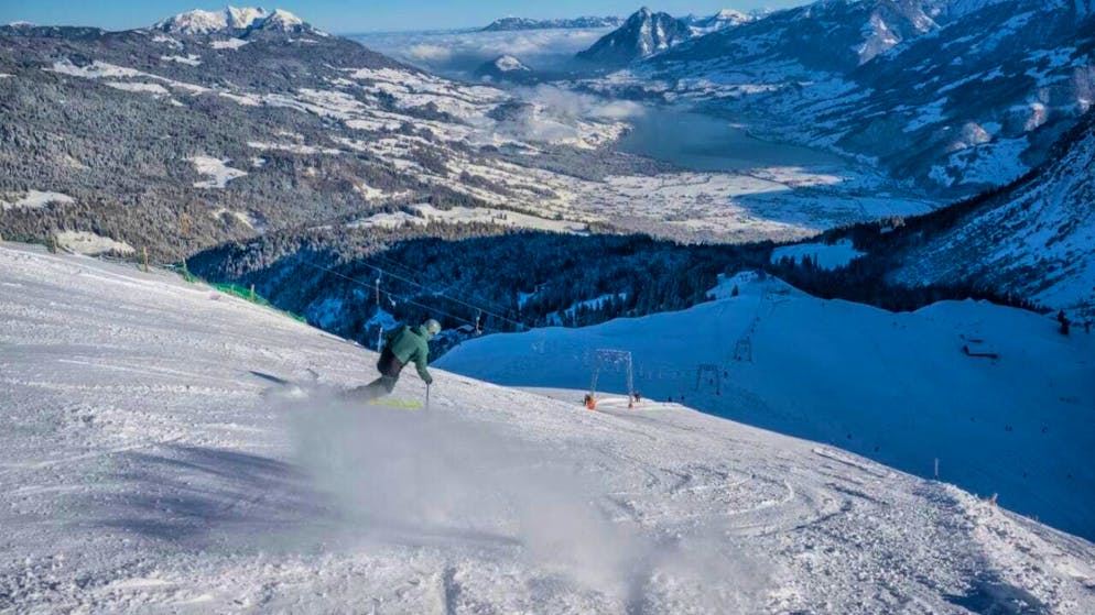 A skier descends a slope at the Mörlialp ski resort in Obwalden Switzerland. Winter sports enthusiasts enjoy the pristine conditions around a charming challet with a snowboarder visible in the distance.