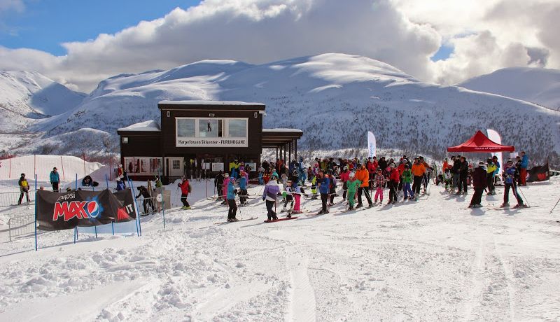 A lively winter scene at Harpefossen ski resort in Western Norway with groups of people and families enjoying various winter sports on the snowy slopes.