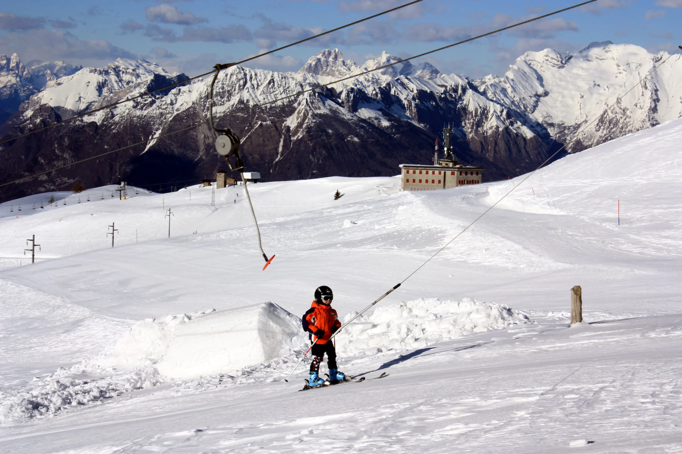 A skier enjoying a brisk run at the Alpe del Nevegal winter sports centre in Nevegal, Italy. The scene captures the charm of the ski resort with a cosy chalet in the background.