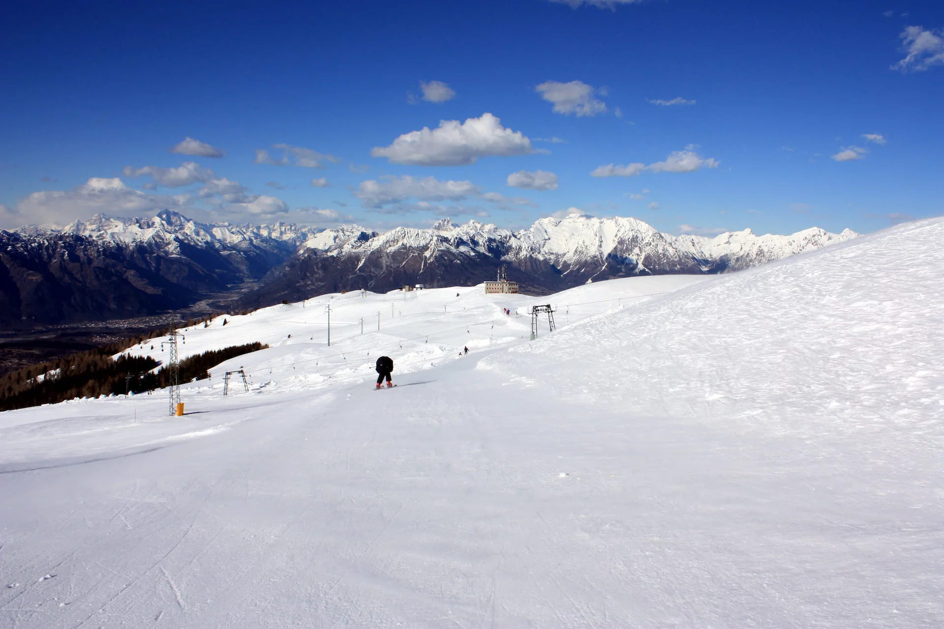 Winter scene at Alpe del Nevegal, Italy. Featuring a skier on the slopes, a charming chalet in the background, and picturesque views of the ski resort.