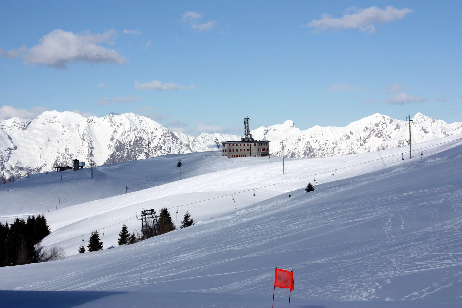 A picturesque view of Alpe del Nevegal ski resort in Italy featuring a charming chalet snow-covered slopes busy with winter sports activities.