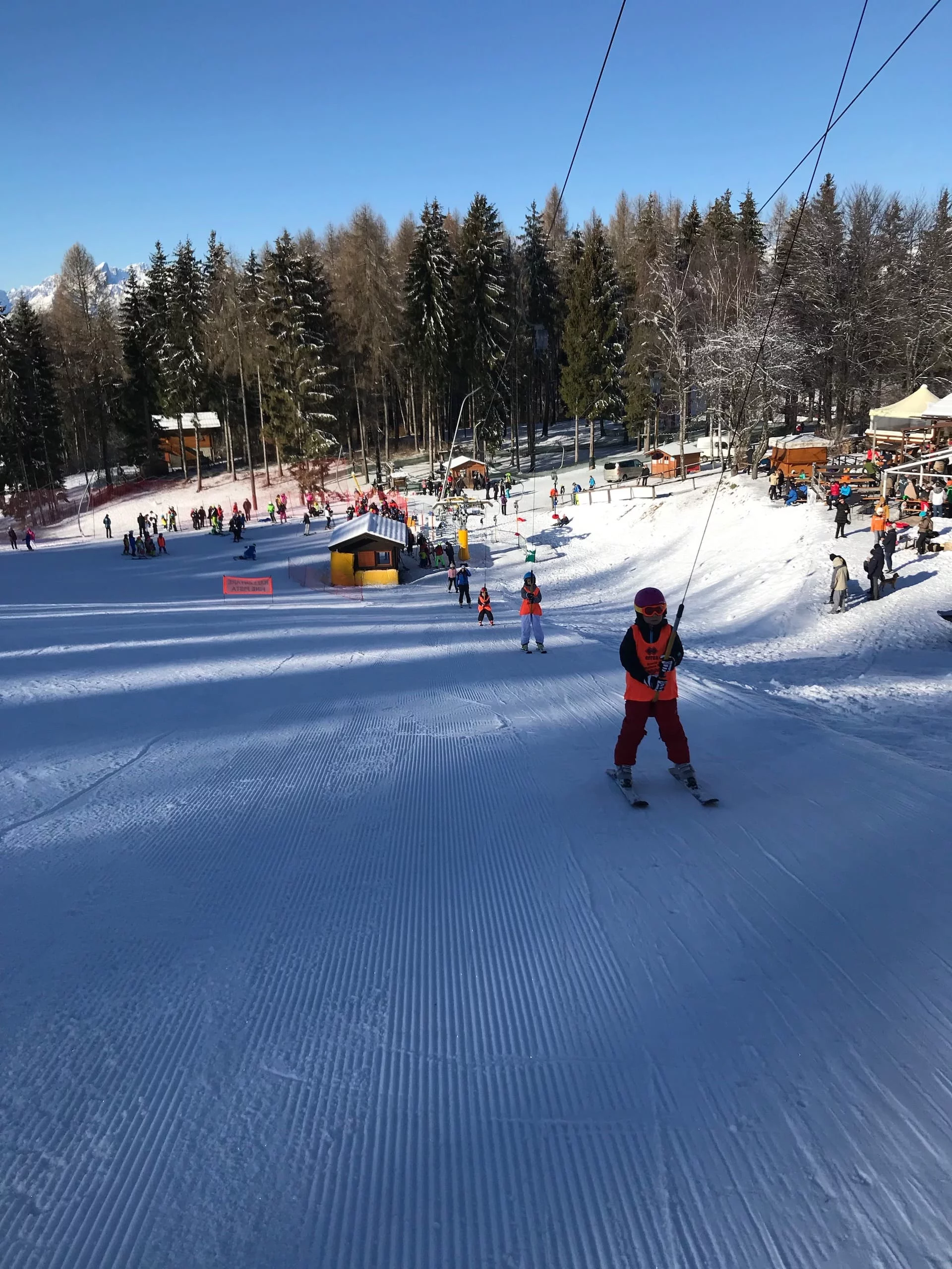 A skier gracefully gliding down a snowy hill at Alpe del Nevegal in Italy, surrounded by the bustling activity of a winter sports centre complete with a welcoming chalet nestled in the background.