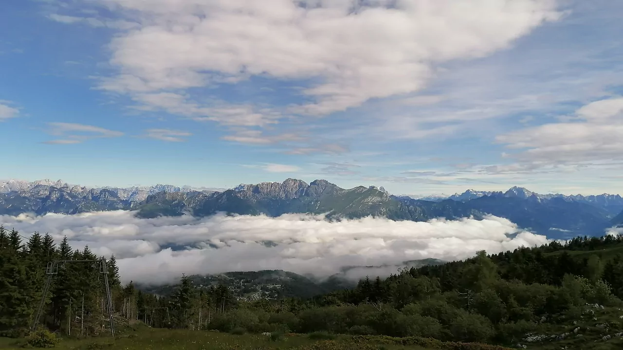 A picturesque chalet sits nestled amidst the vibrant green landscape of the Alpe del Nevegal mountain range in Nevegal, Belluno, Italy on a sunny day. A mountain bike leans next to the chalet, adding a touch of adventure to this tranquil scene.