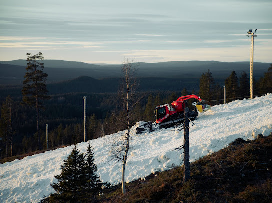A winter sports scene in Kåbdalis Northern Sweden featuring a snowmobile and a skier against a backdrop of snowy slopes and a ski lift.