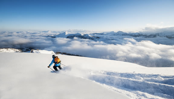A skier is gliding down a slope at Zauchensee | Flachauwinkl in Pongau, Salzburg, Austria. The breathtaking winter sports scene also includes a glimpse of a chalet and other parts of the ski resort.
