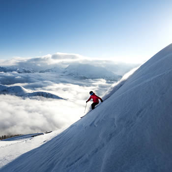 A skier skillfully glides down the snowy slopes of Zauchensee-Flachauwinkl a popular ski resort in Pongau Salzburg Austria with mountains in the backdrop and a few snowboarders in the vicinity.