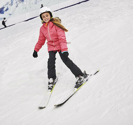 A skier and a child learning to ski at The Snow Centre in Hemel Hempstead, England. Winter sports scene featuring a snowboarder also, all within a winter sports centre.