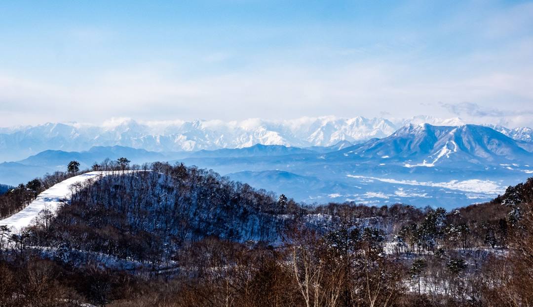 A stunning winter scene at Shigakogen Hasuike in Nagano, Japan, featuring a picturesque snowy mountain and winter sports activity happening amidst the serene landscape.
