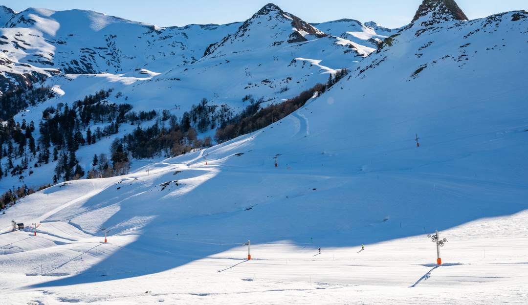 Winter scene at Hautacam ski resort in France featuring a chalet, skiers, and a sports center amidst a snowy landscape.