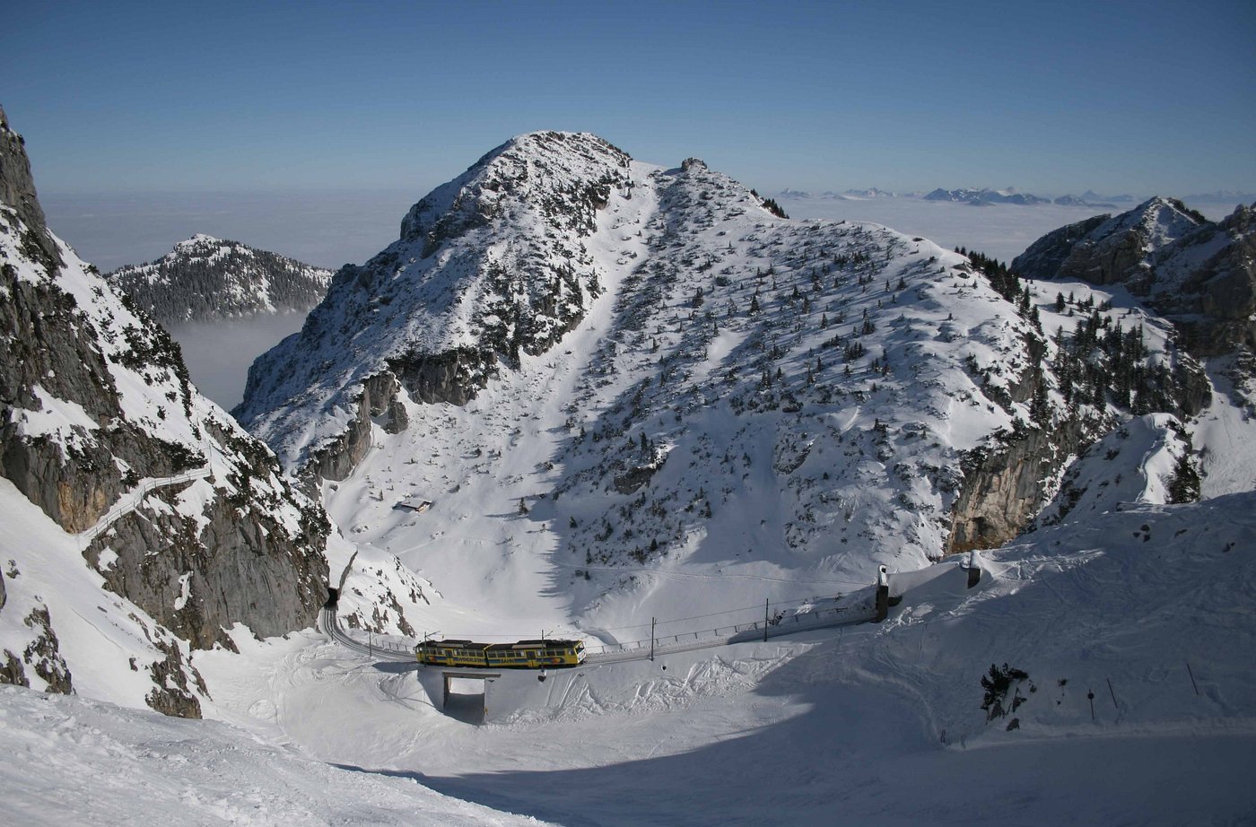 Ski resort at Wendelstein in Brannenburg, Bavaria, with a cozy challet and a mountain hut in sight, offering a welcoming winter sports scene amidst the snow-clad landscape.