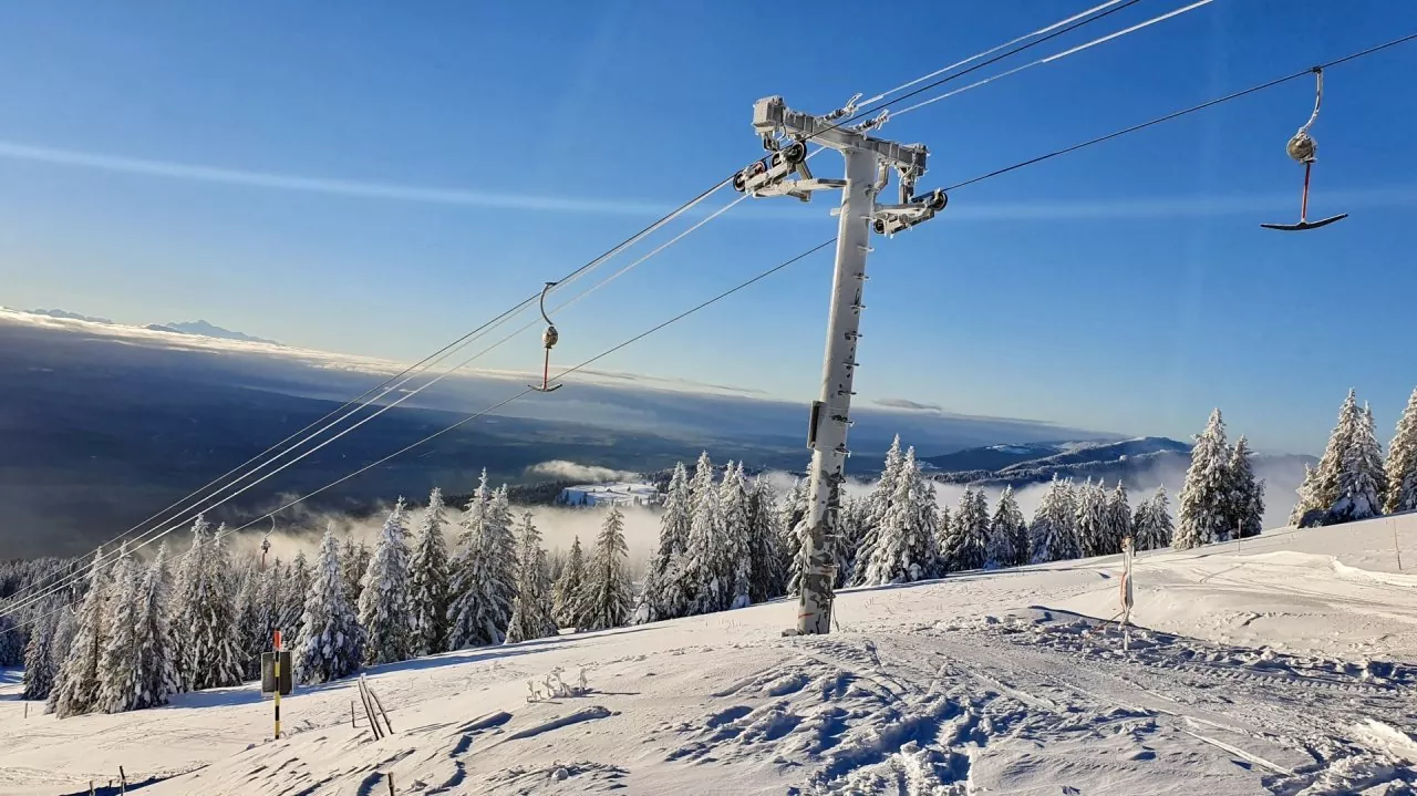 Ski lift ascending a snowy mountain in Ste-Croix - Les Rasses, Switzerland. Skiers enjoying winter sports on well-groomed fields a part of a popular ski resort. Breathtaking winter landscape in the background.