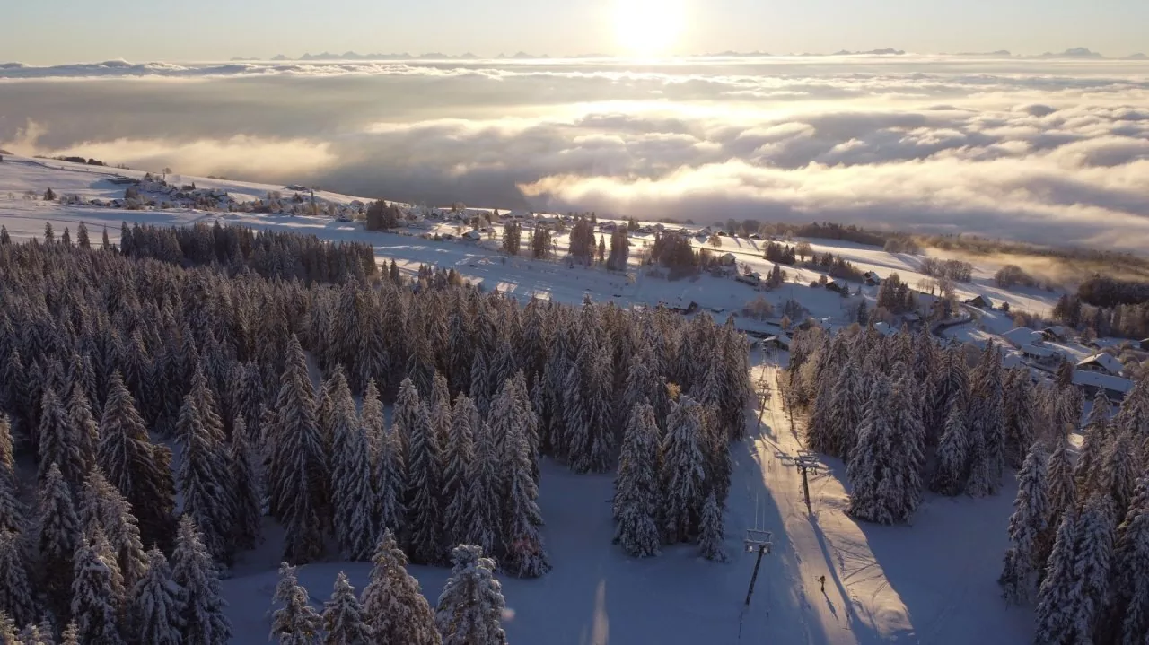 Winter sports enthusiasts enjoying activities at Ste-Croix - Les Rasses Ski Resort in Switzerland, surrounded by a mesmerizing winter scenery under a clear sky.