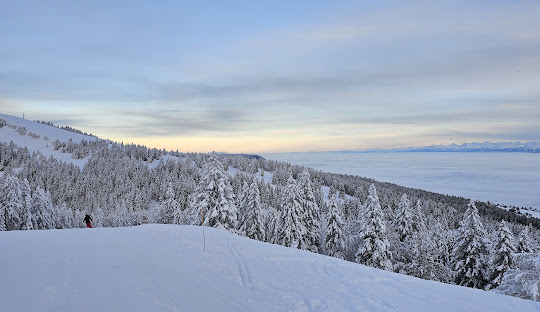 Winter scene in Ste-Croix - Les Rasses, Switzerland, depicting snowy slopes bustling with winter sports activities amidst chalets and a ski resort.