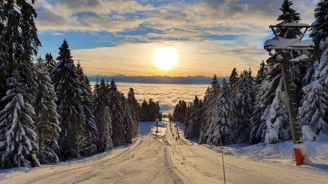 Winter sports enthusiasts enjoy the snowy slopes of Ste-Croix - Les Rasses in Switzerland, with charming chalets nestled amongst the pristine landscape, under a clear, sunny sky.