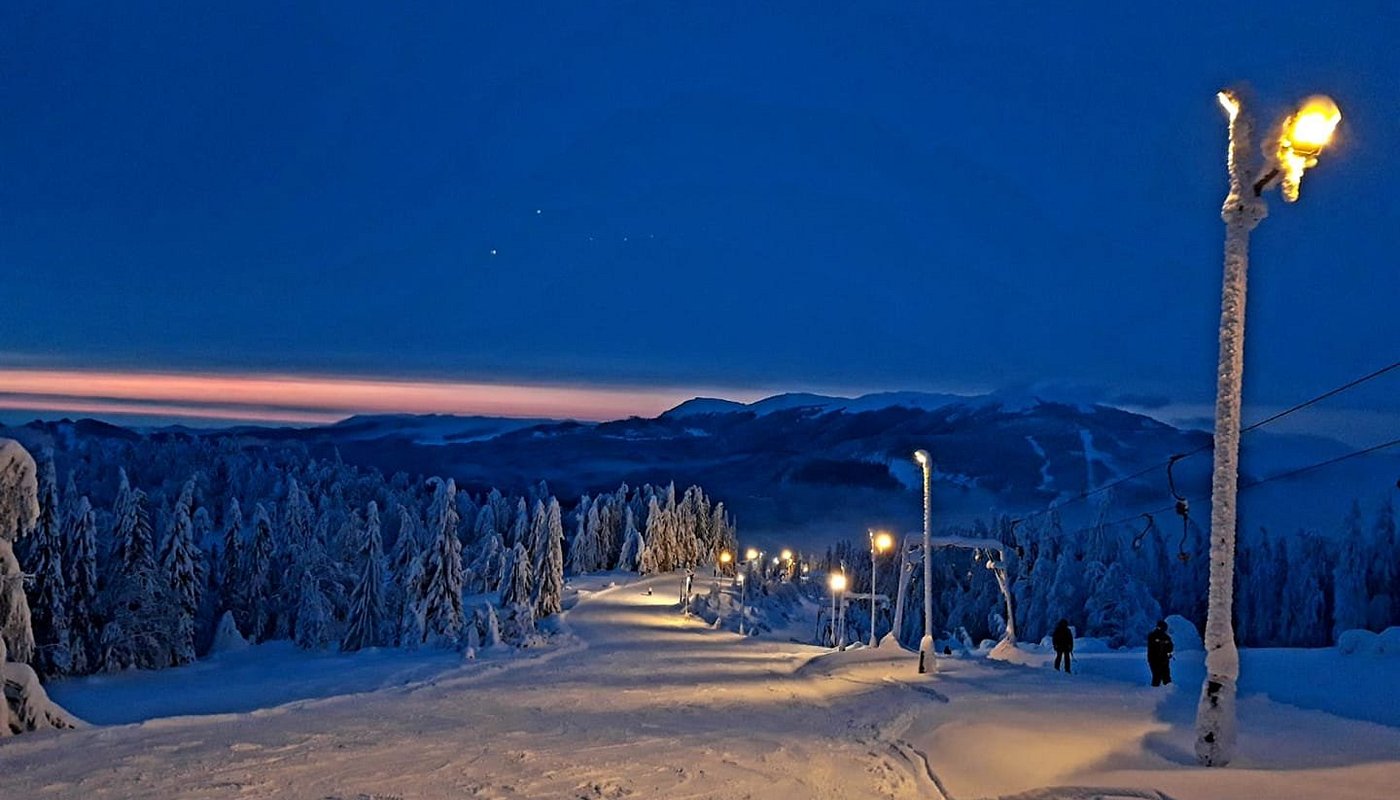 A picturesque view of the Superski Roata Cavnic in Romania showcasing a bustling ski resort amid a stunning winter scenery. Skiers can be seen enjoying winter sports with a ski lift visible nearby.