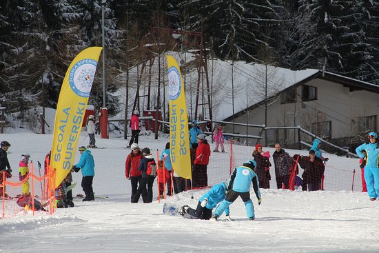 Winter sports scene at Superski Roata Cavnic in Romania, highlighting a skier navigating snowy terrain with a winter sports centre, chalet, and ski resort visible in the distance.