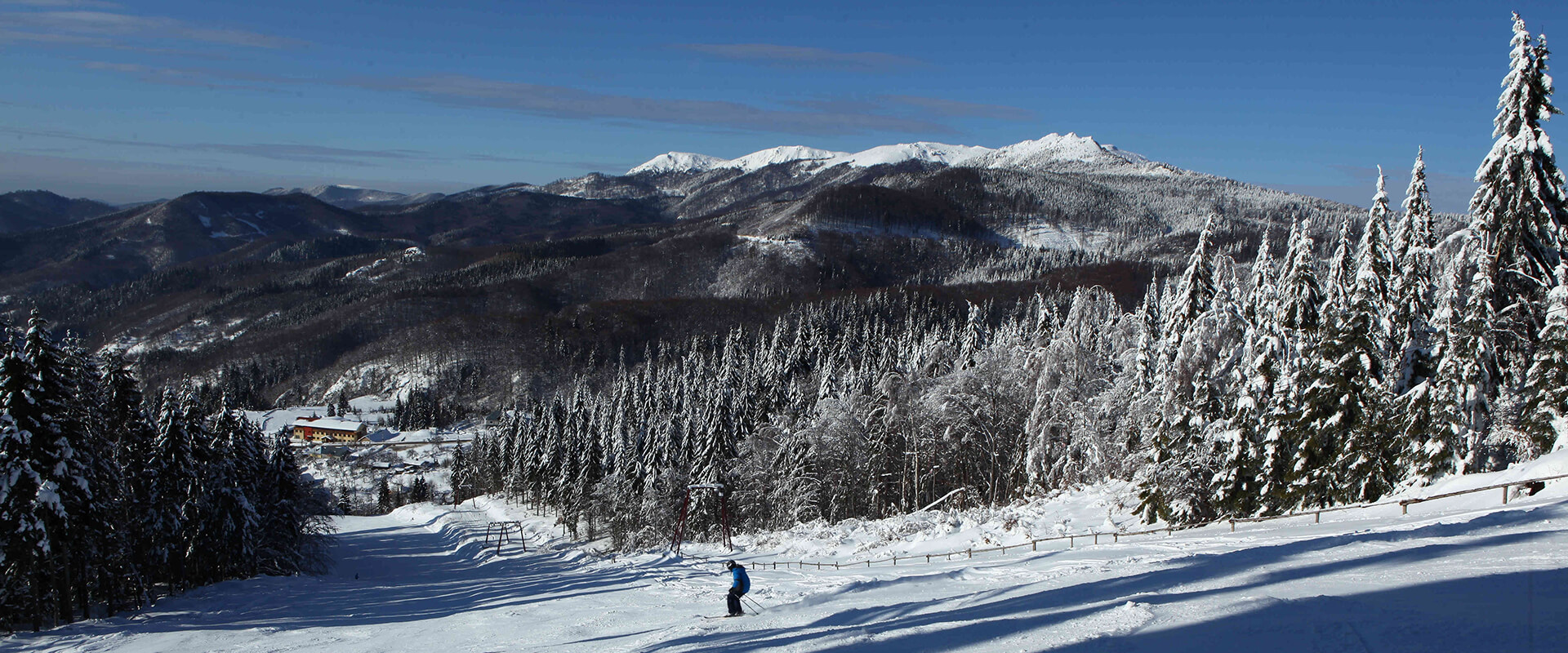 A skier descending a slope at Superski Roata Cavnic, a Romanian ski resort. A stunning winter landscape surrounds the area, highlighted by a quaint chalet nestled among the snow.