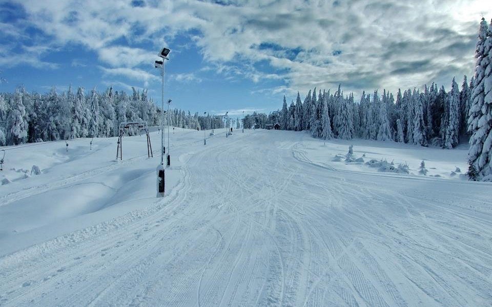 Winter scene at Superski Roata Cavnic in Romania featuring bustling ski resort with ski lift and snowmobile, surrounded by snowy mountains and sports enthusiasts.