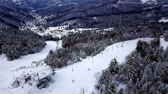 Winter scene at Superski Roata Cavnic in Romania, highlighting a bustling ski resort with skier-clad slopes and a charming chalet nestled amidst stunning snowy scenery.