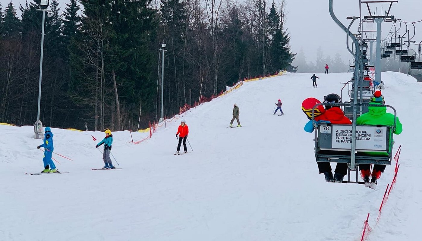 Winter sports enthusiasts enjoying a day of skiing at Superski Roata Cavnic ski resort in Romania, featuring skiers gliding down snowy slopes under a clear blue sky.