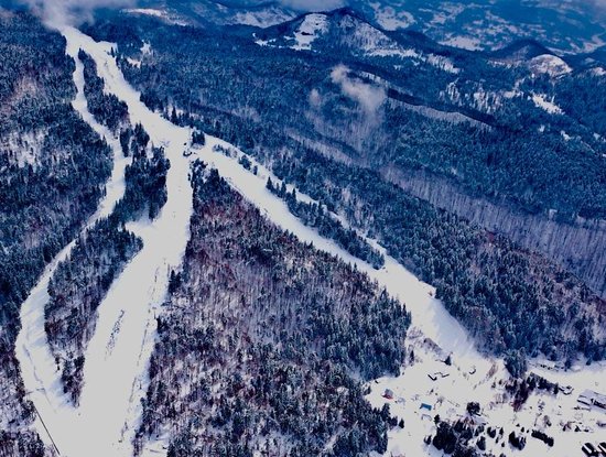 Winter scene at Superski Roata Cavnic in Romania, featuring bustling snow-covered slopes, a ski lift carrying enthusiasts to the top, and a cozy chalet nestled in the scene.