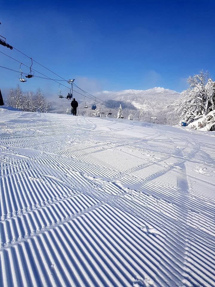 Skier gliding down snowy slopes at Superski Roata Cavnic in Romania with challet and ski lift in the backdrop portraying a dynamic winter sports scene.