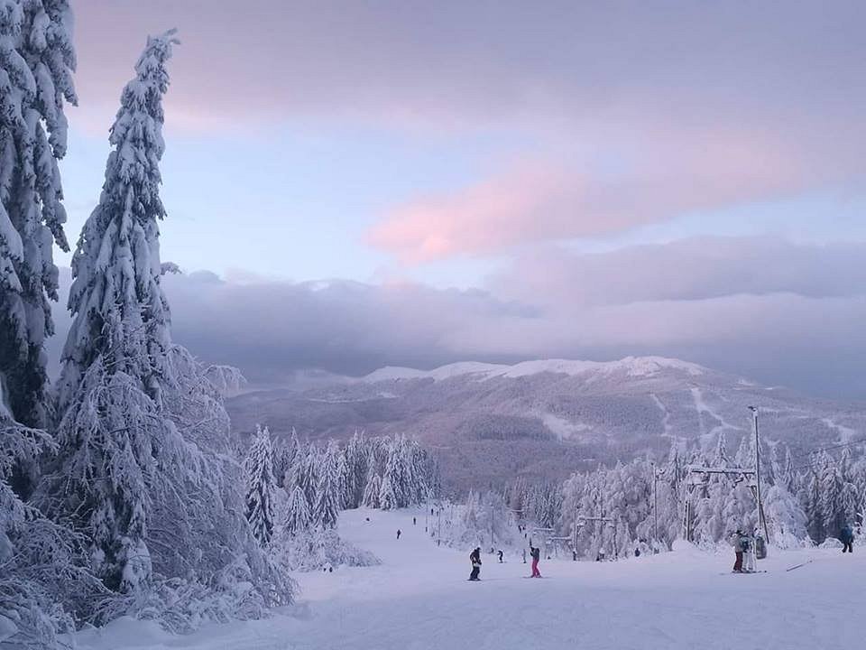 Scenic view of Superski Roata Cavnic in Romania with skiers enjoying winter sports, featuring a ski resort against a beautiful winter backdrop and a ski lift in operation.