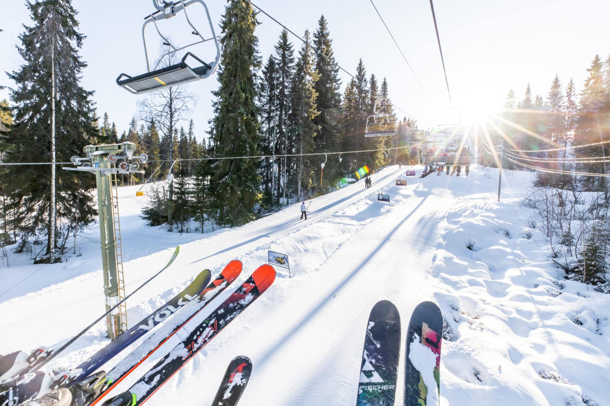 Skiers enjoying a sunny day at the Vuokatti ski resort in Kainuu East Finland. A ski lift transports people up the snowy slopes while a skier makes their way downhill.