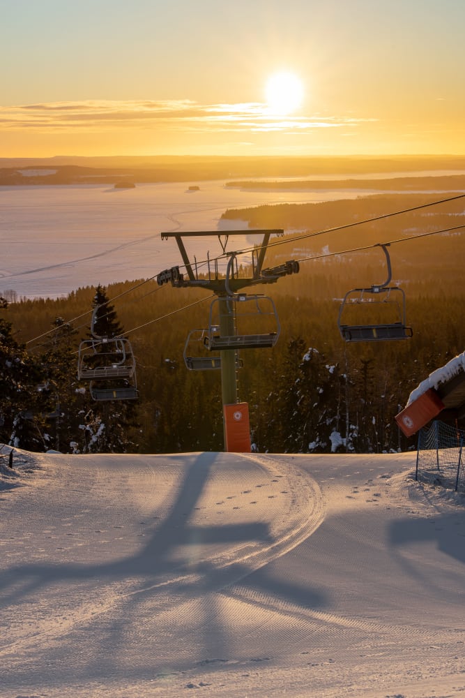 A skier and snowboarder enjoying a winter day in Vuokatti East Finland. The ski lift in the background takes more sports enthusiasts up the snow-covered mountain in this popular ski resort.