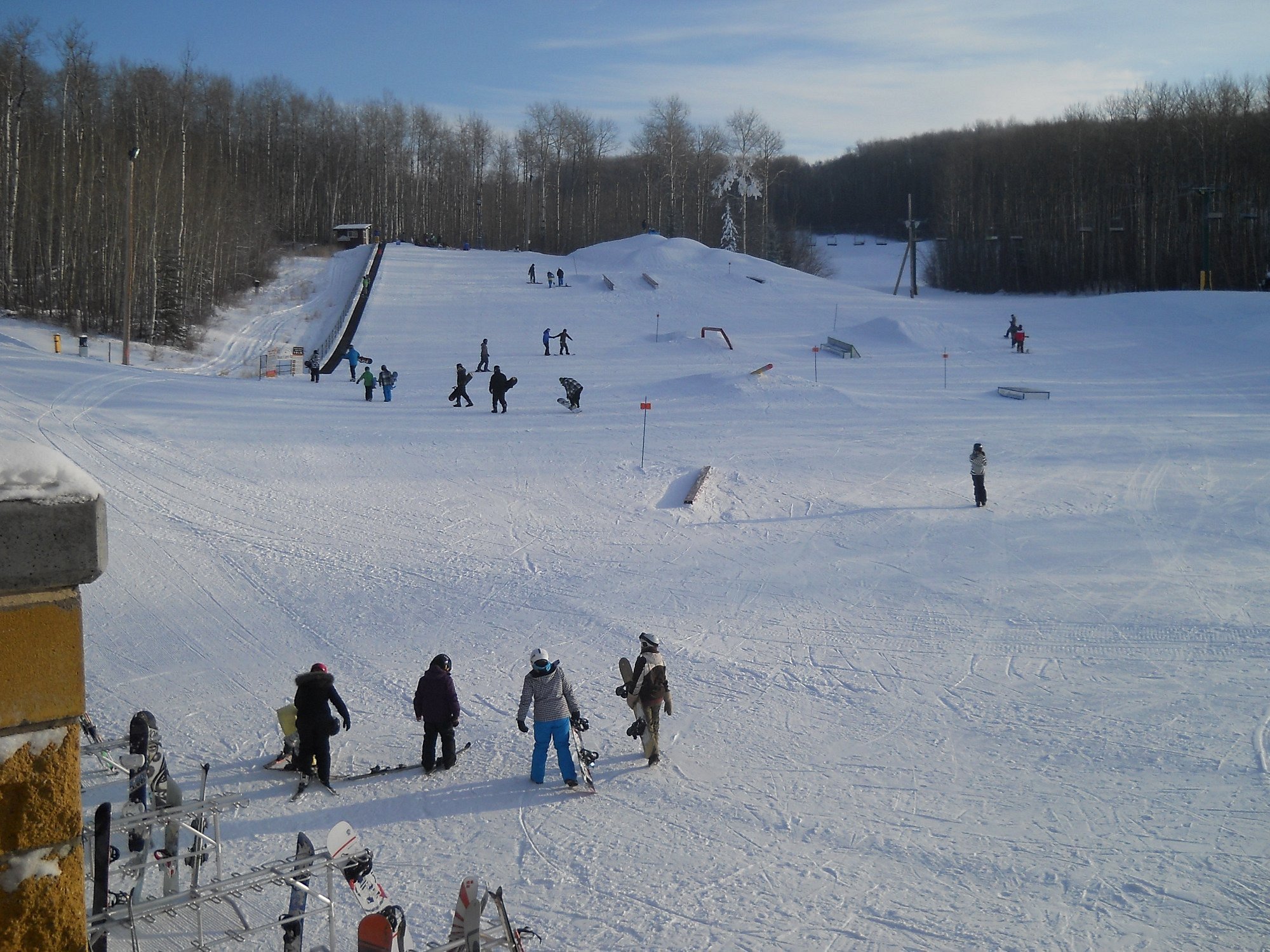 Winter sports scene at Kinosoo Ridge, Alberta with a bustling ski resort in the background. A ski lift carries eager skiers uphill while a few others glide down the snowy slopes.