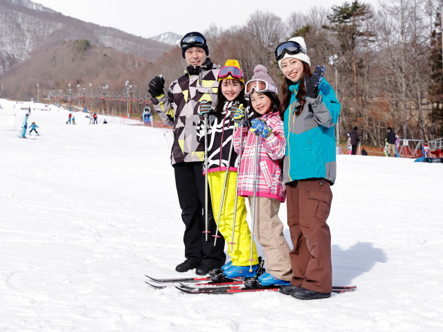 A family enjoying a day of skiing at the Jiigatake ski resort in Honshu, Japan. The scene is a typical winter sports setting, filled with people skiing down the snow-covered slopes.