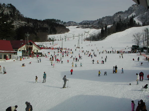 A snow-covered ski resort at Mikawa Onsen, with a winter sports scene going on. A chalet and a ski lift can be seen in the background, nestled amidst the tranquil landscape of Chūbu, Niigata, Japan.