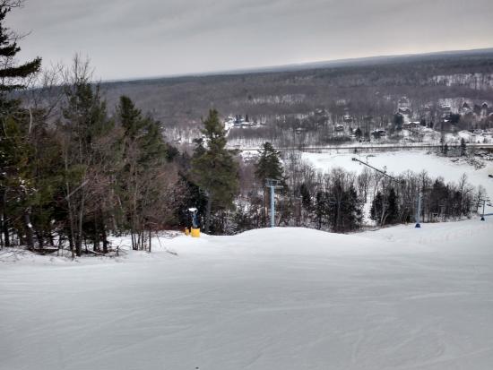 Winter scene at Calabogie Peaks, Ontario, featuring bustling activity at a ski resort. Skiers fill the slopes and a ski lift, with a charming chalet nestled among the snow-covered trees.