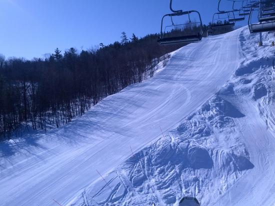 A skier glides down a slope at Calabogie Peaks in Ontario, Canada, with a ski lift and chalet stationed among snow-laden trees, painting a lively winter sports scene at the ski resort.