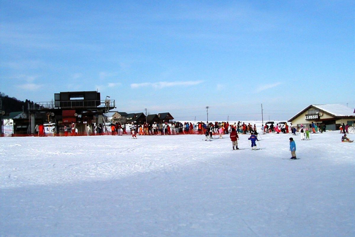 A busy winter scene at Itsukamachi Ski Resort in Niigata Japan featuring multiple skiers navigating the snowy terrain complete with a ski centre and chalet in the background.