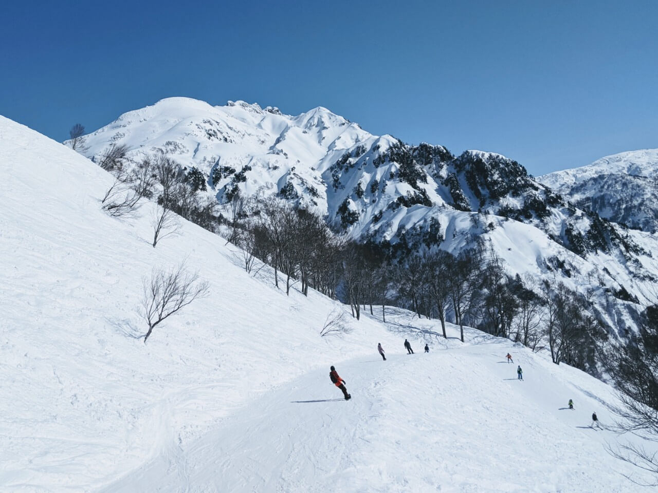 Hakkai Sanroku Ski Area in Japan - a group of people skiing down a snow covered mountain.