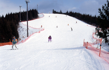 Winter sports scene at Taiheizan Opas in Japan with a sports centre in sight skiers on the slope and a chalet in the background.
