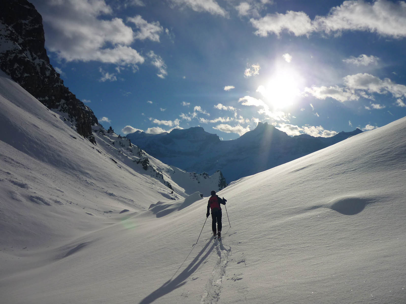 A winter sports scene in Biel-Kinzig, Uri, Switzerland featuring a skier in mid-action on a snowy slope with a quaint challet in the backdrop amidst beautiful winter scenery.