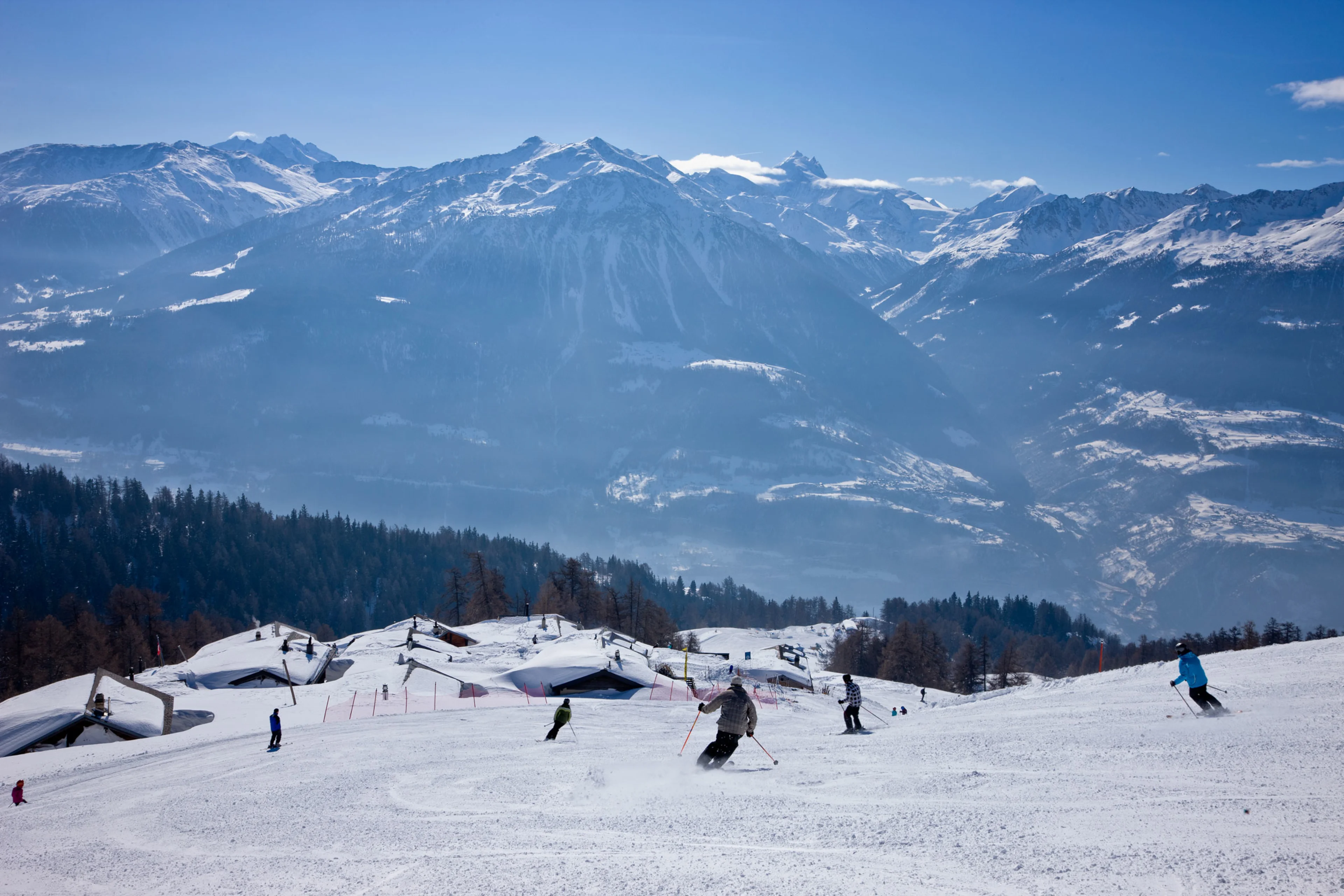 A bustling winter sports scene at Sportbahnen Gampel-Jeizinen a ski resort in Switzerland filled with groups of people enjoying skiing and snow activities.