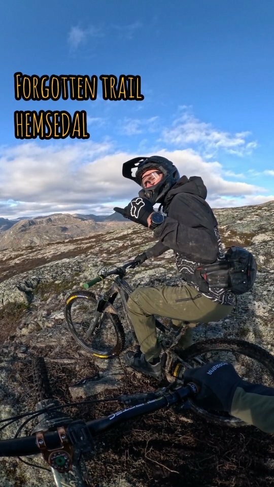 A mountain bike is prominently featured in the foreground of a scenic Hemsedal landscape in Norway. In the backdrop, there is a challet nestled at the foot of a majestic mountain.