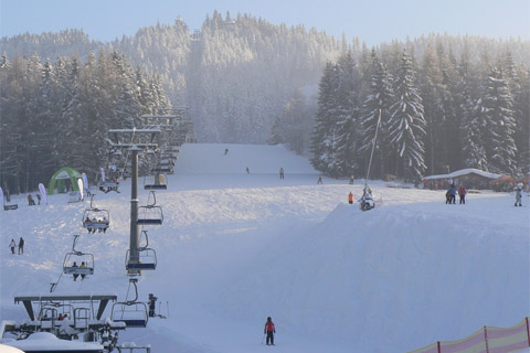 A ski resort in Špičák Šumava-Železná Ruda Czech Republic bustling with winter sports enthusiasts. A ski lift ascends the snow-covered mountain near a cozy challet.