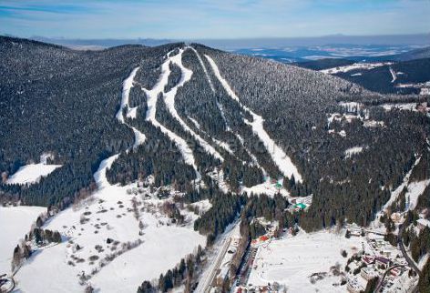 Image of a bustling ski resort in Špičák Czech Republic featuring skiers enjoying winter sports a ski lift in operation and a quaint chalet tucked among trees.