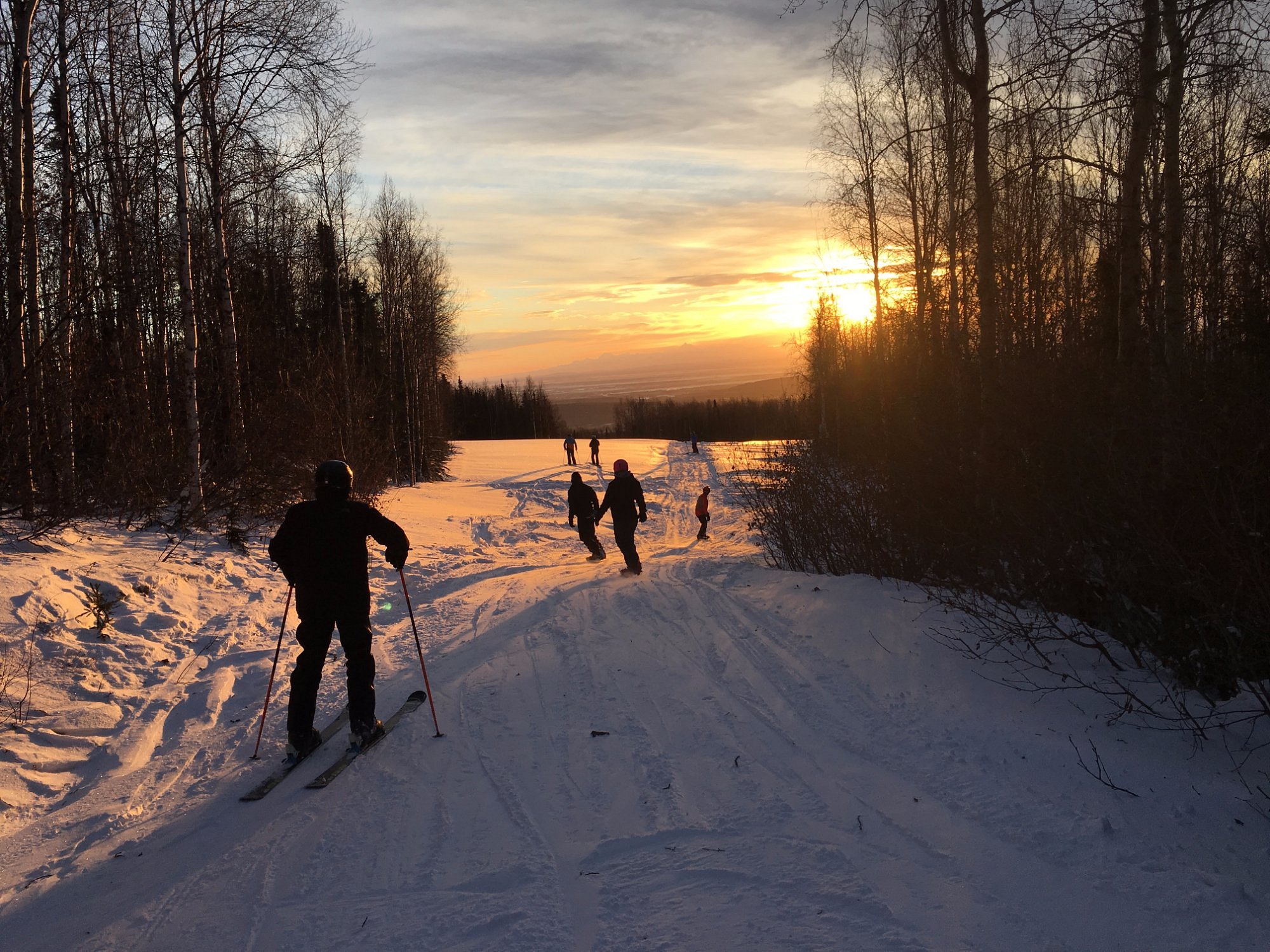A winter sports scene at Moose Mountain in Fairbanks Alaska showcasing the dazzling winter scenery. Skiers potentially a family navigate the white slopes while a sports center is subtly visible in the background.