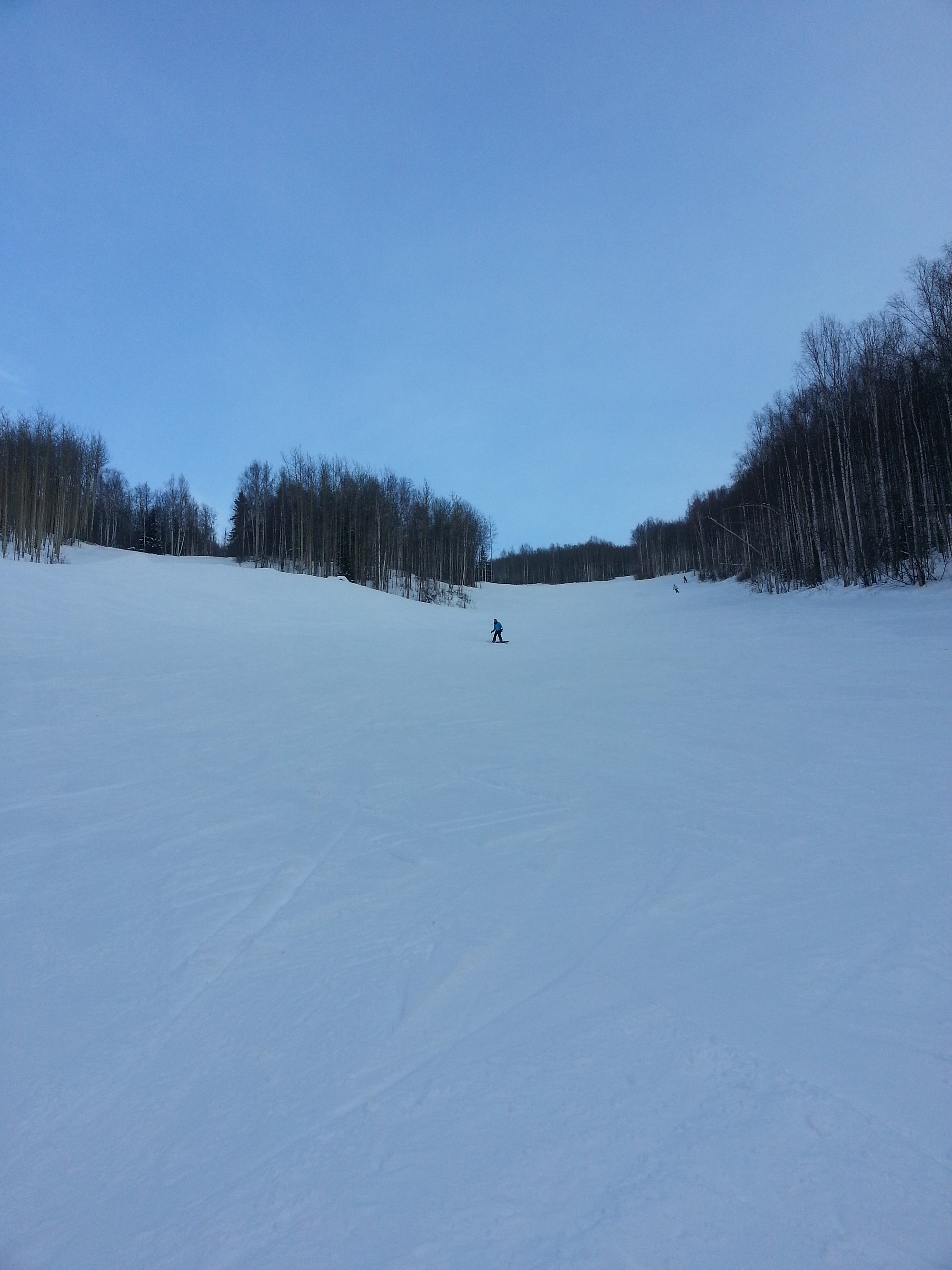 A picturesque winter view at Moose Mountain Fairbanks Alaska featuring a charming chalet nestled among snowy peaks. Skiers enjoy the slopes - an idyllic ski resort scene complete with a ski lift.
