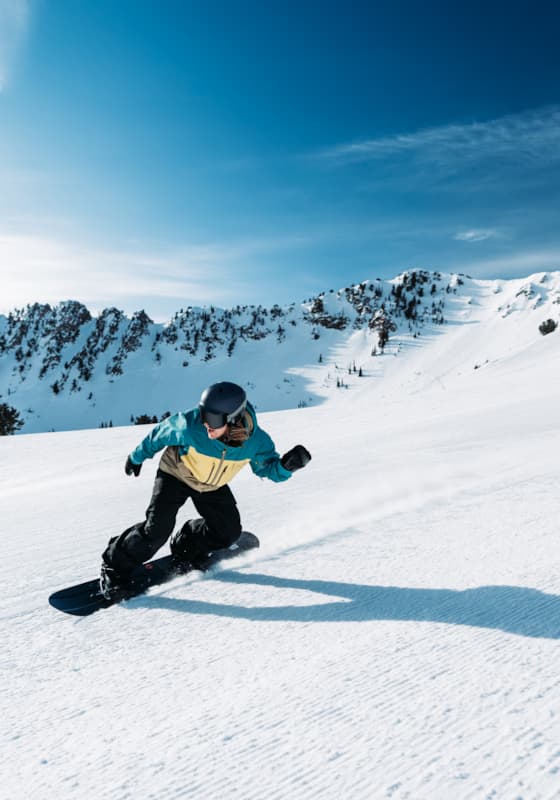 A snowboarder shredding the snowy slopes at Snowbasin resort in Utah. The world around him seems to pause as he carves his way down the mountain, leaving a trail of snow dust behind him.