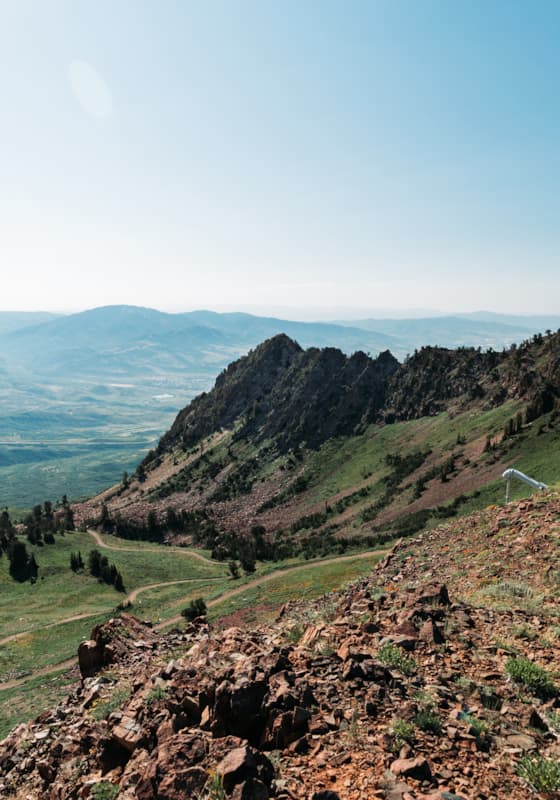 View of Snowbasin in Utah showcasing a prominent mountain in the backdrop, with a mountain biker and a chalet nearby. The scenic beauty of a ski resort and a ski lift subtly complete the scene.