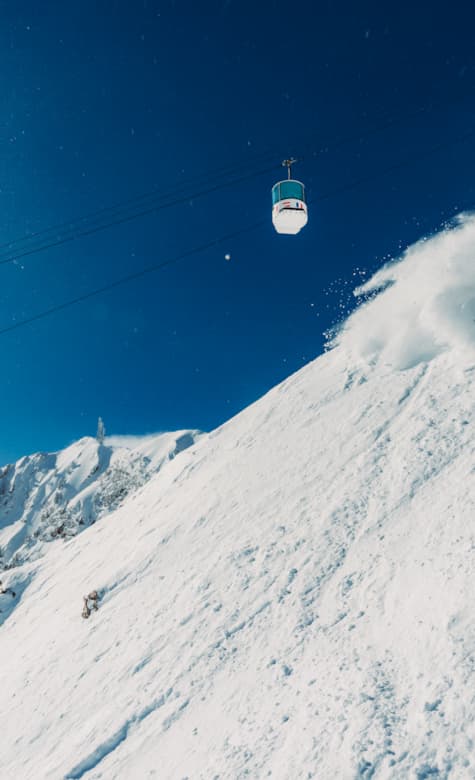 A skier enjoys a picturesque winter scene at Snowbasin in Utah USA. The ski lift ascends over the vibrant resort indicating a bustling vacation spot for ski enthusiasts. A quaint chalet is subtly nestled in the snow-kissed landscape.