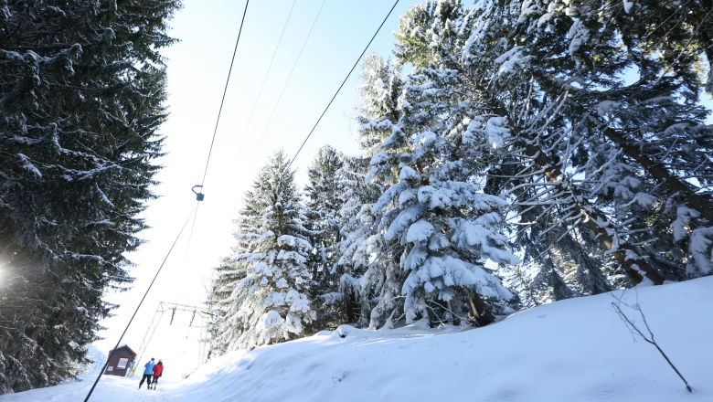 A skier enjoying a downhill run in Ski & Bike Park Königsberg Austria with a ski lift visible in the background. Snowmobile and ski resort amenities hint at a thriving winter sports scene.