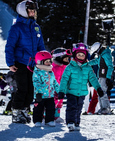 A family including a young child learning are enjoying a day of winter sports at Mont Habitant ski resort in Saint-Sauveur Quebec amid lush snow-capped trees.